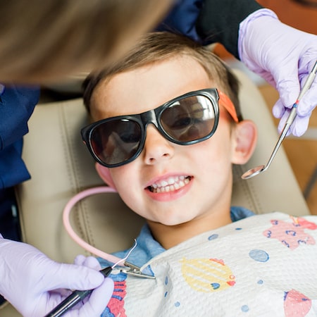 Little boy in the dentist chair wearing sunglasses and smiling